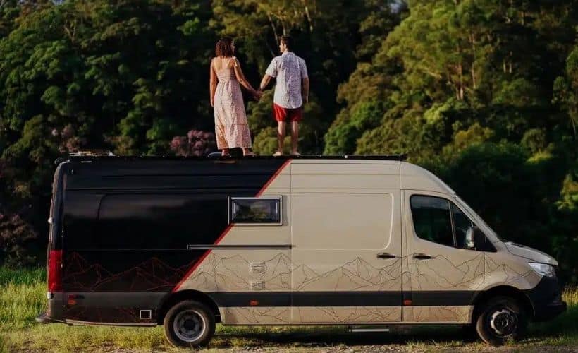 Casal traveleiros em cima de uma van motorhome preto e bege com um mapa topográfico desenhado na parte bege